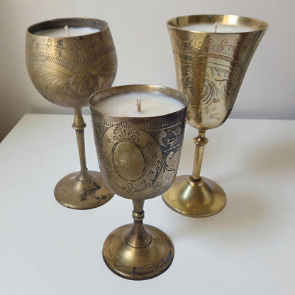 Three ornate brass candle holders with candles inside on a white surface.
