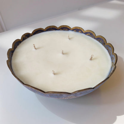 Decorative candle with wicks in a scalloped-edge container on a white surface