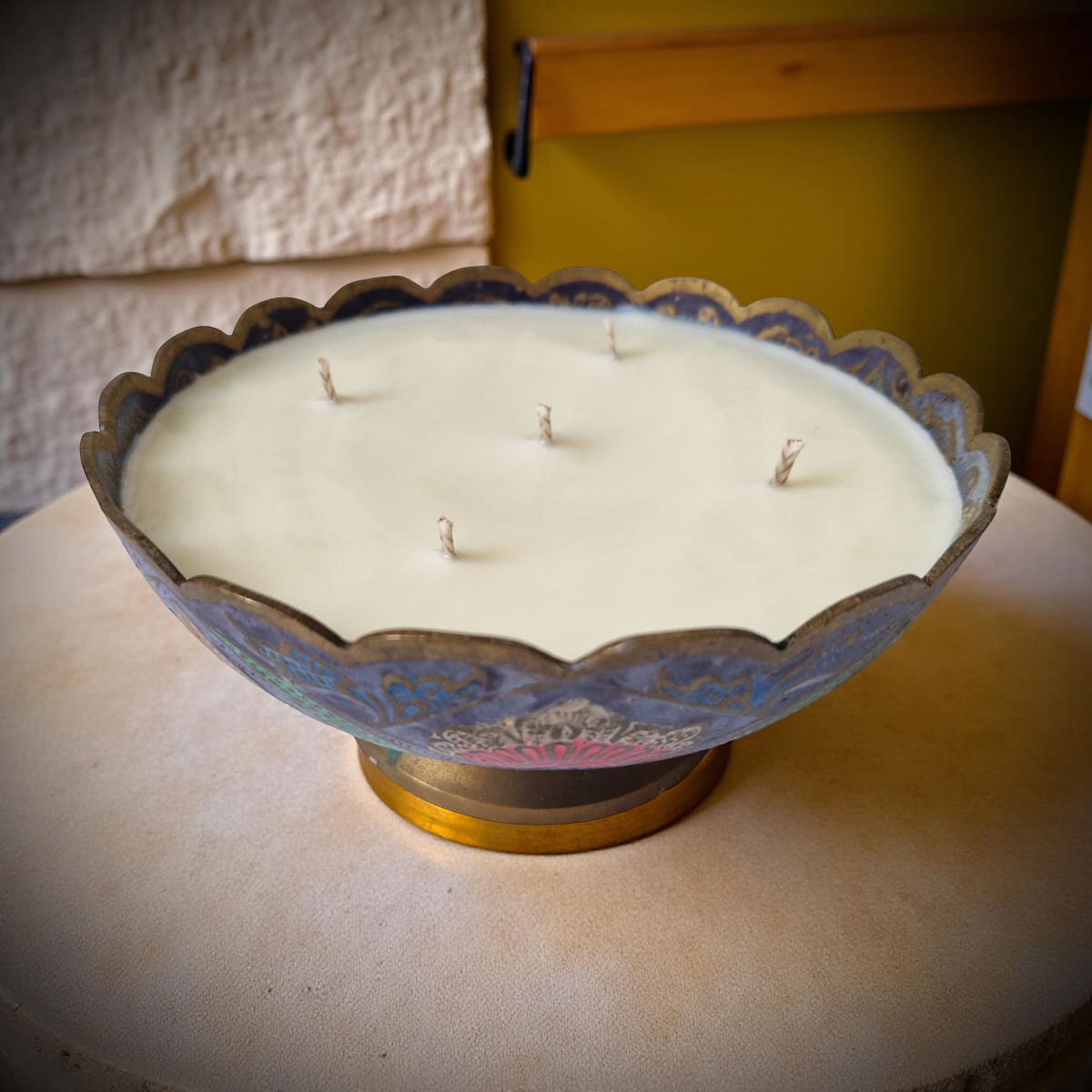 Decorative candle in a scalloped metal holder on a wooden surface