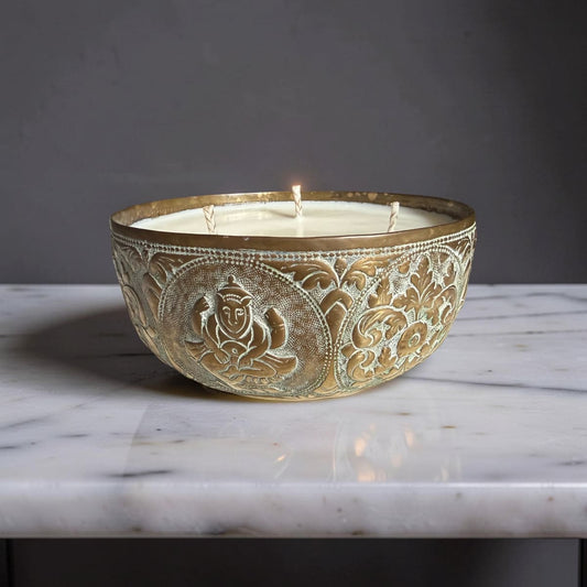 Decorative candle in an ornate metal bowl on a marble surface with a dark background