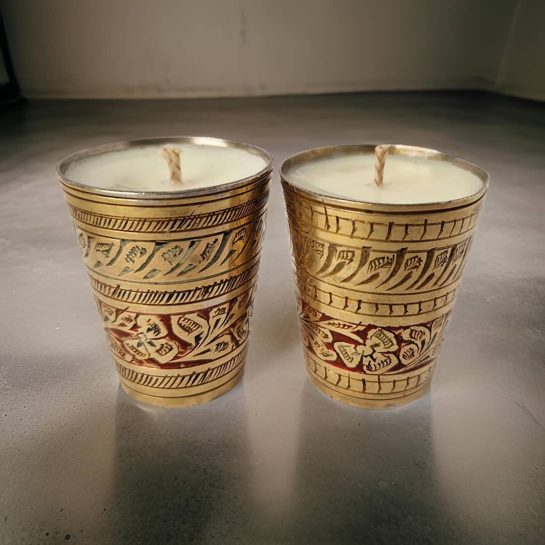 Two ornate candles in decorative holders on a reflective surface.