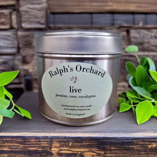 Candle tin labeled 'Ralph's Orchard' with green leaves on a wooden surface