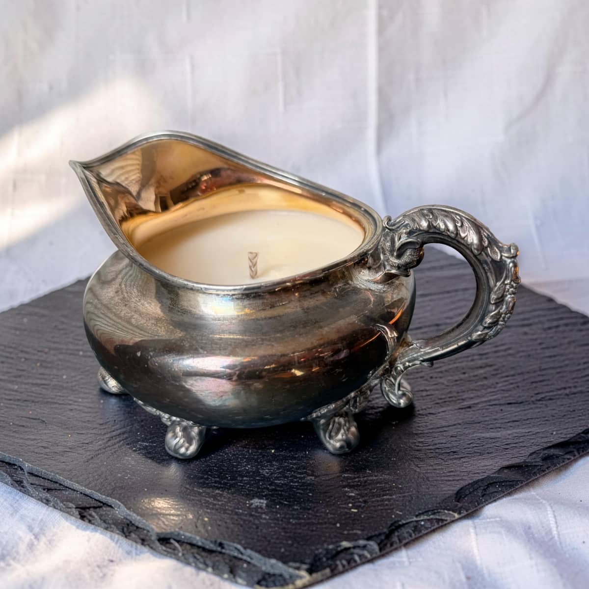 Silver gravy boat with candle inside on a dark slate surface