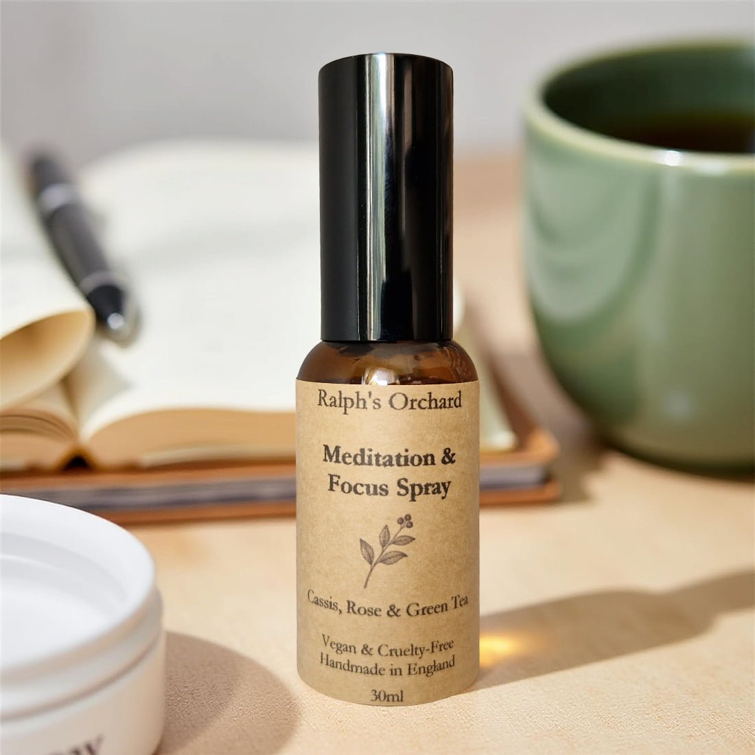 Bottle of Ralph's Orchard Meditation & Focus Spray on a table with a book and mug in the background