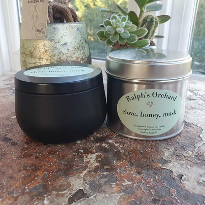 Two candles from Ralph's Orchard on a textured surface with plants in the background