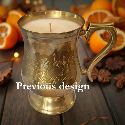 Decorative candle in a gold holder with oranges and cookies on a wooden surface