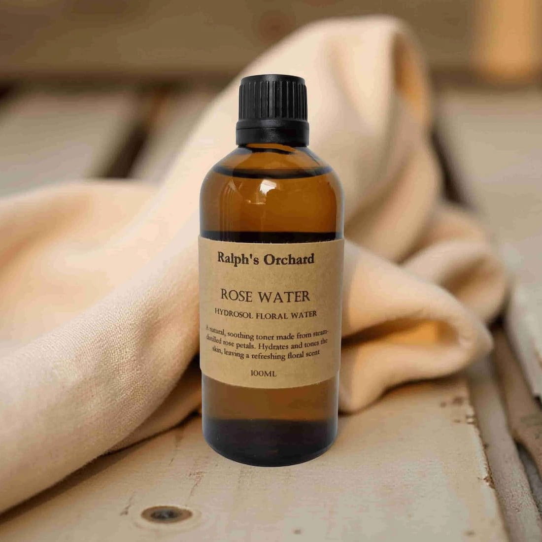 Bottle of Ralph's Orchard Rose Water on a wooden surface with a beige cloth.