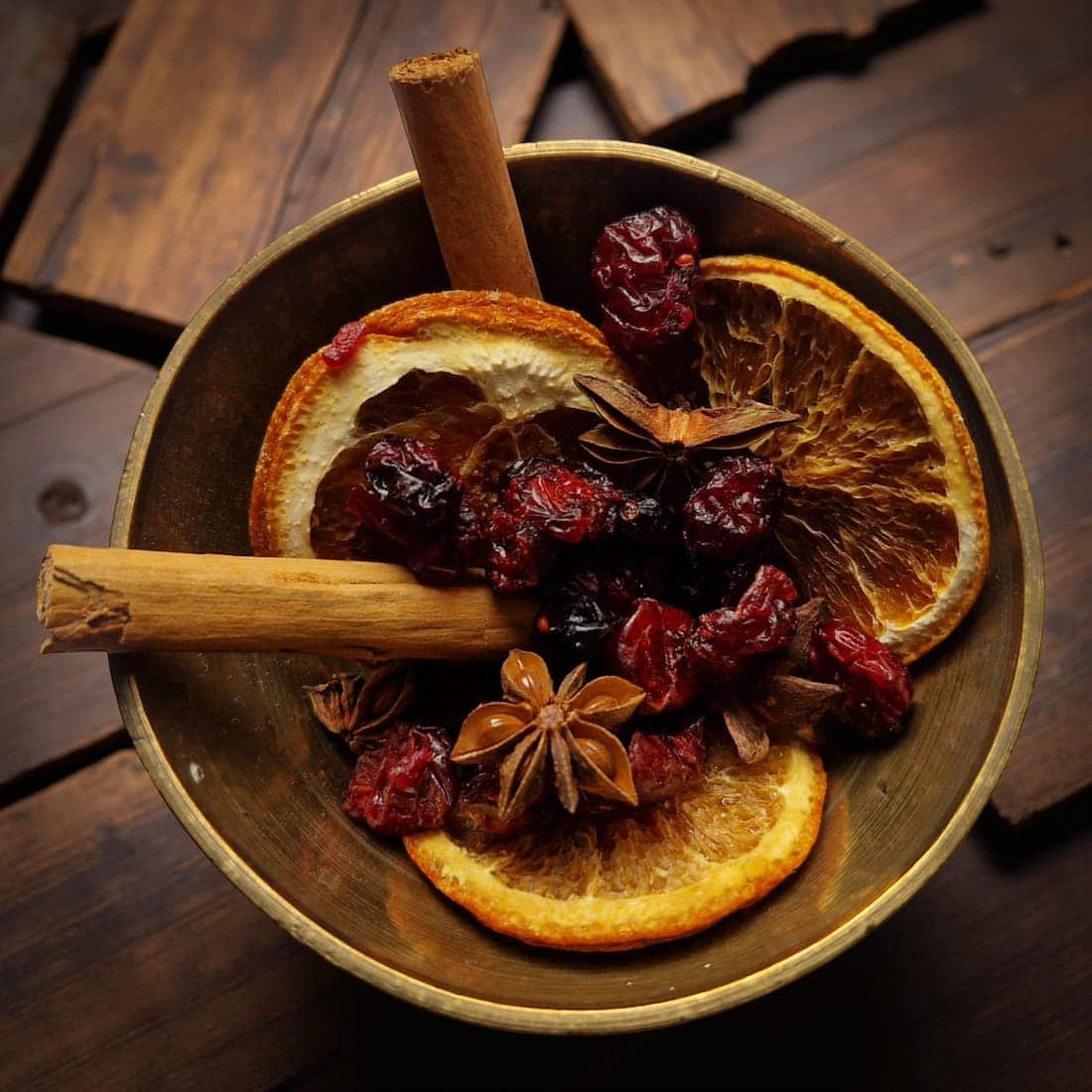 Wooden bowl with dried fruits, oranges, and cinnamon sticks on a wooden surface