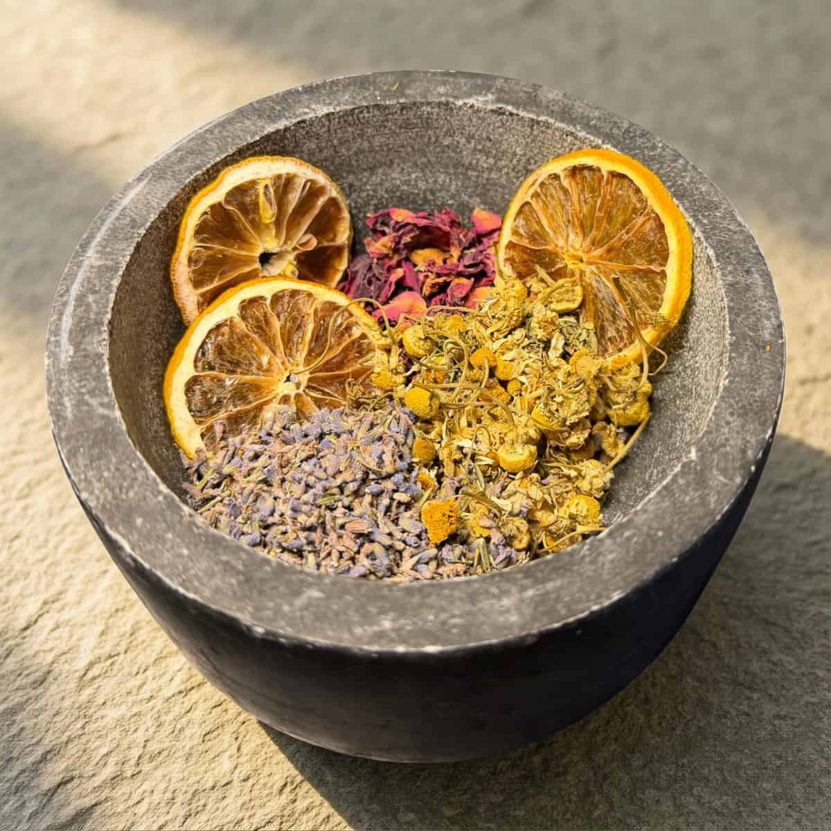Mortar with dried herbs and citrus slices on a stone surface