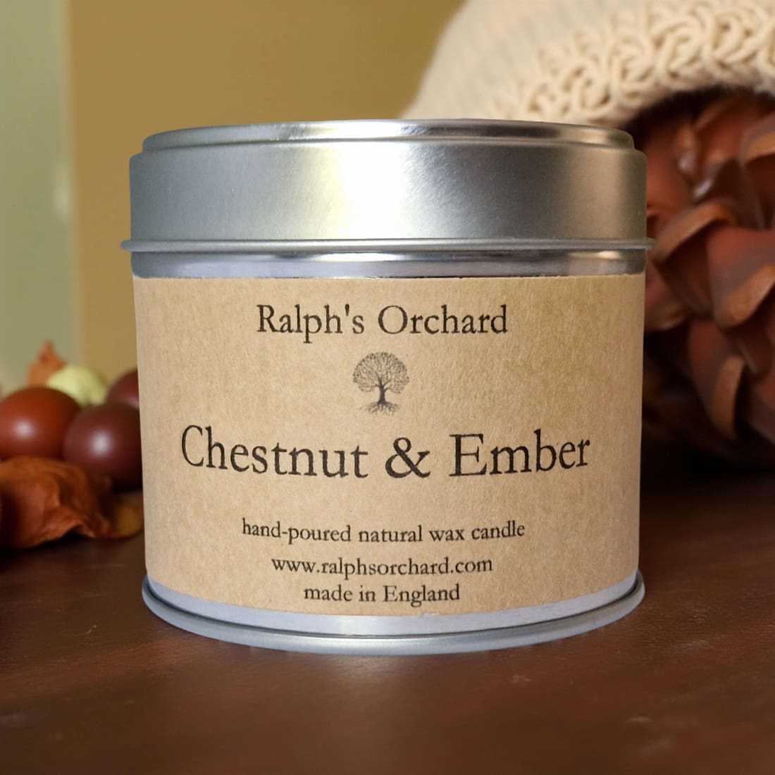 Candle tin labeled 'Ralph's Orchard Chestnut & Ember' on a wooden surface with autumn decorations.