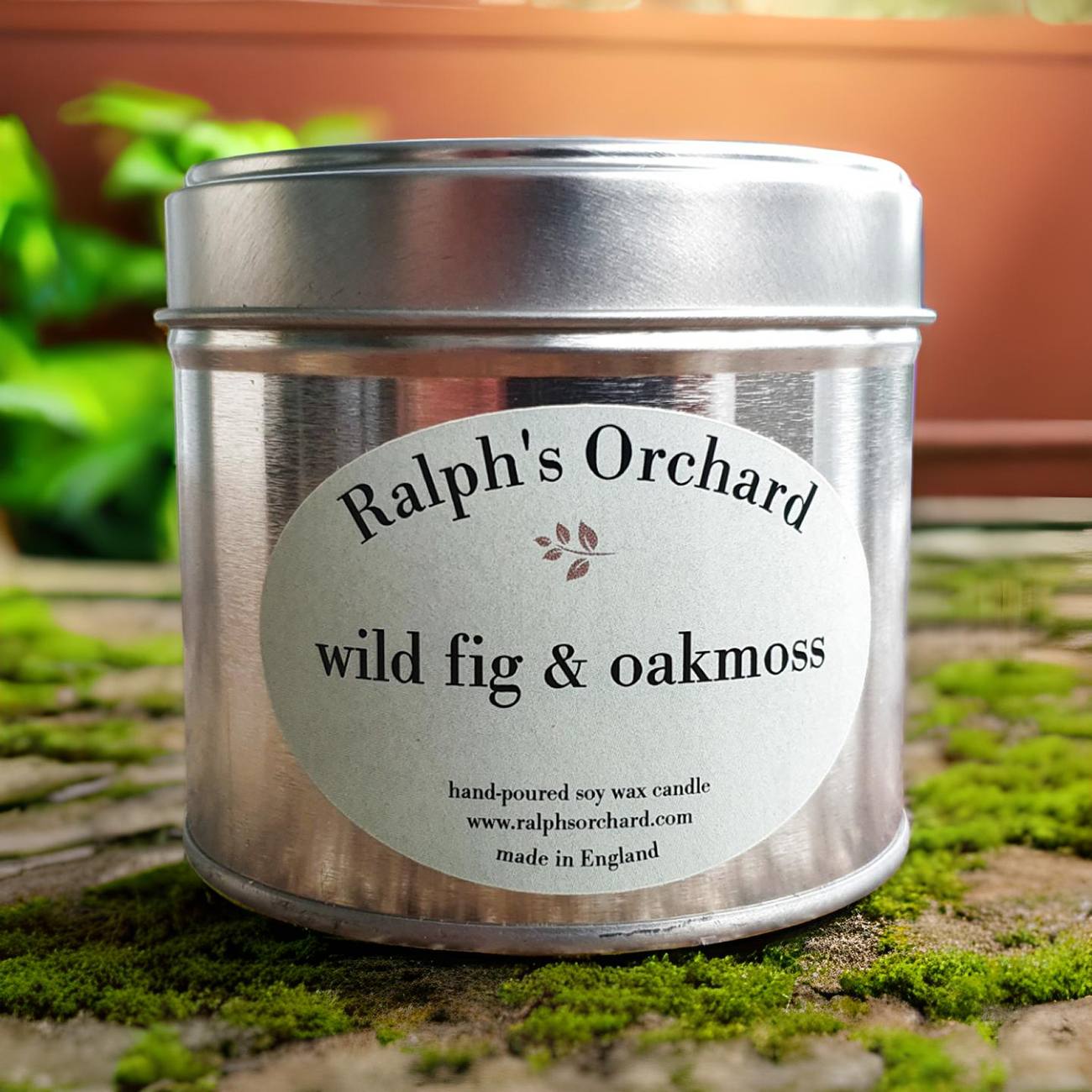 Candle tin labeled 'Ralph's Orchard wild fig & oakmoss' on a natural background