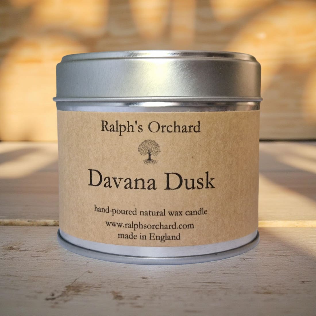 Candle in a tin labeled 'Davana Dusk' by Ralph's Orchard on a wooden surface.