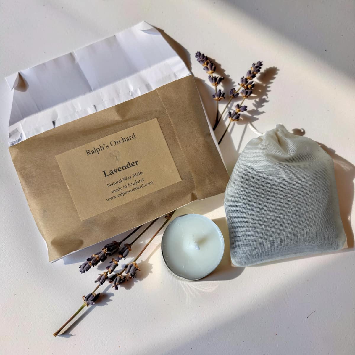 Lavender soap bar with packaging, candle, and lavender sprigs on a light surface