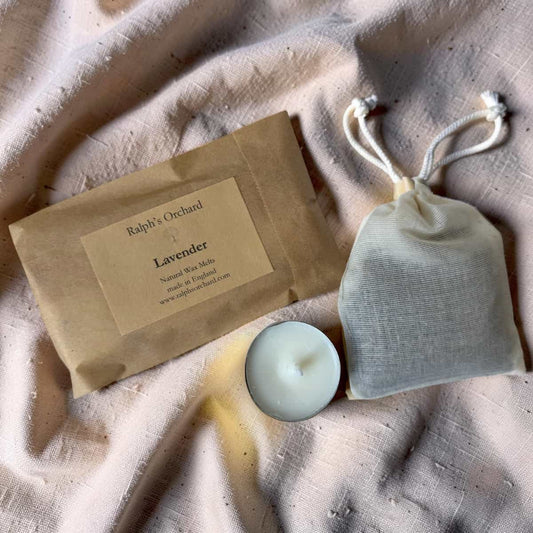 Bar of soap and candle with 'Ralph's Orchard' label on a textured fabric background