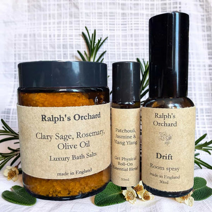 Three Ralph's Orchard products including bath salts, essential oil roll-on, and room spray on a white background with greenery.