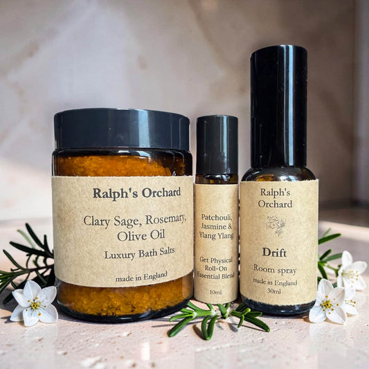 Three bottles of Ralph's Orchard products on a light surface with flowers and greenery.