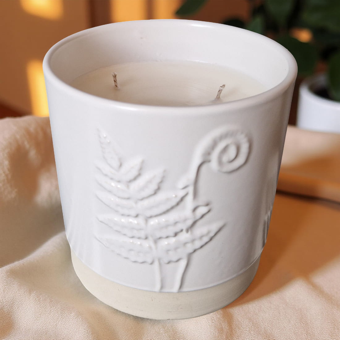 White ceramic candle holder with embossed design on a beige surface