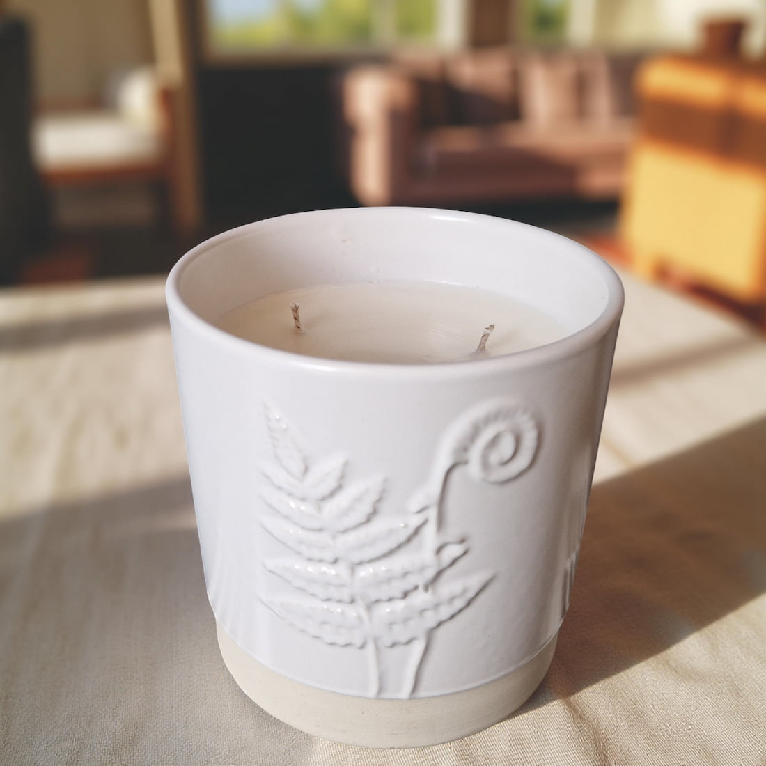 White ceramic candle with embossed design on a surface, blurred indoor background