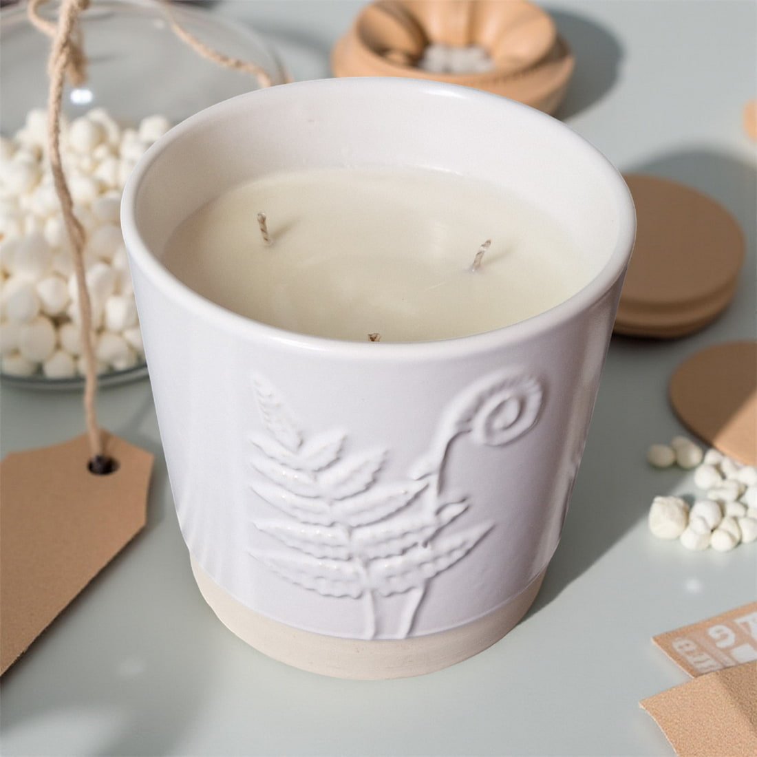 White ceramic candle with embossed design on a light gray surface