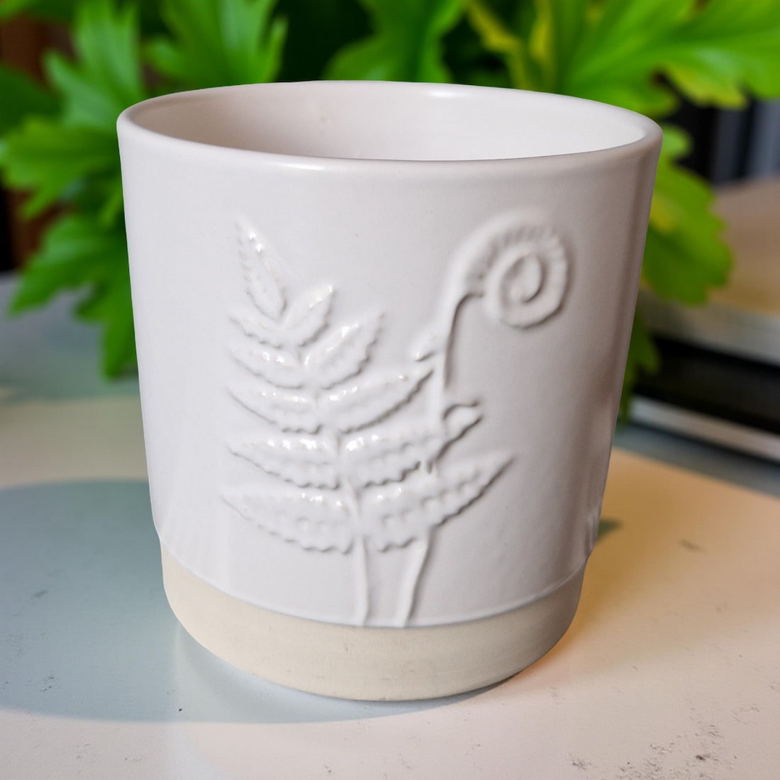 White ceramic cup with embossed design on a surface with greenery in the background