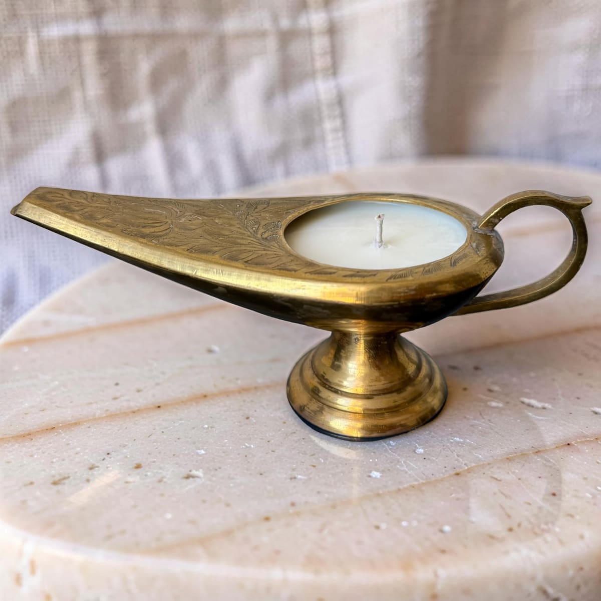 Brass lamp-shaped candle holder on a marble surface with a neutral background