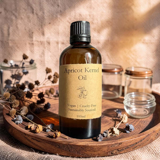 Bottle of apricot kernel oil on a wooden tray with dried plants and jars.
