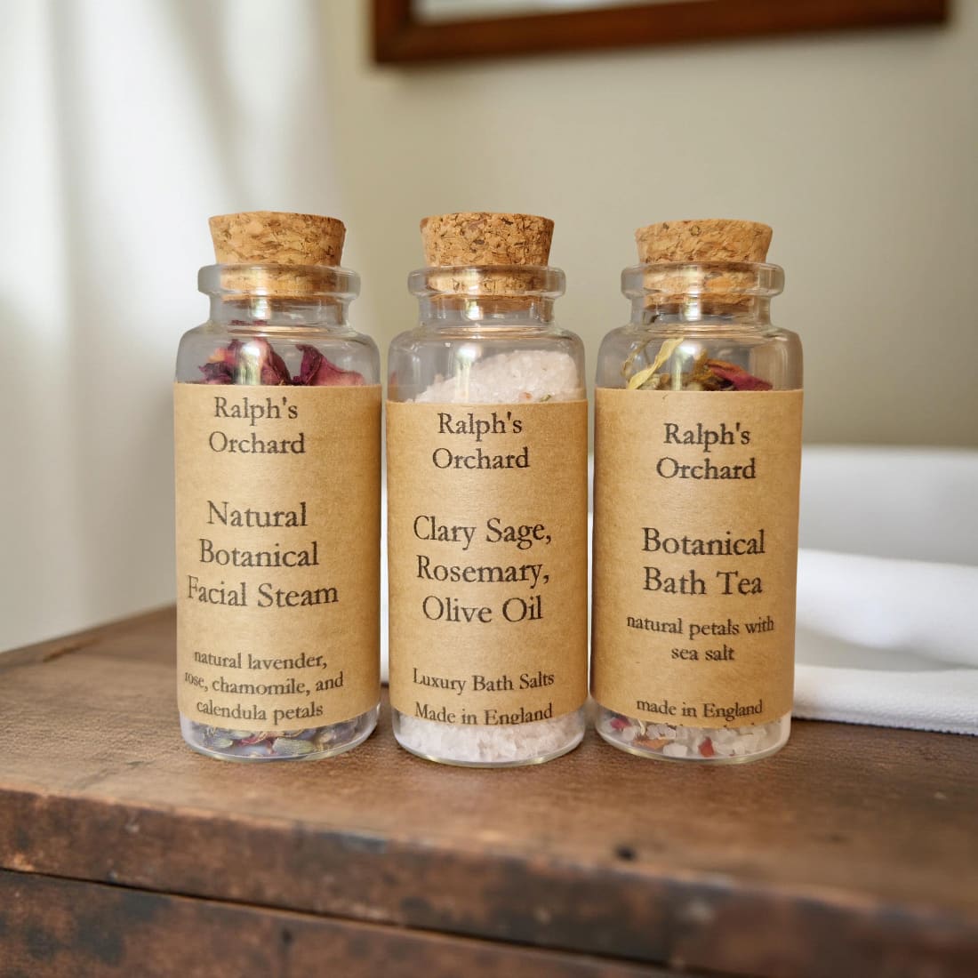 Three glass bottles with cork lids labeled 'Ralph's Orchard' on a wooden surface.