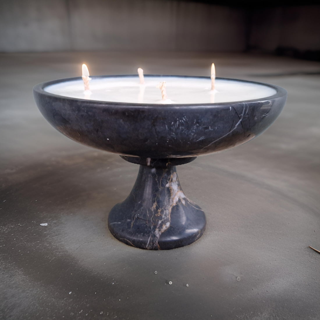 Black marble candle holder with three lit candles on a concrete surface