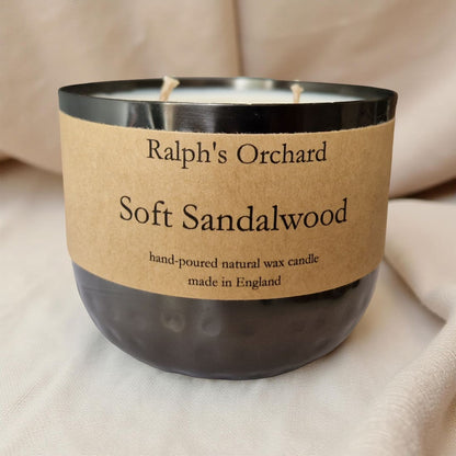 Candle labeled 'Ralph's Orchard Soft Sandalwood' on a beige fabric background