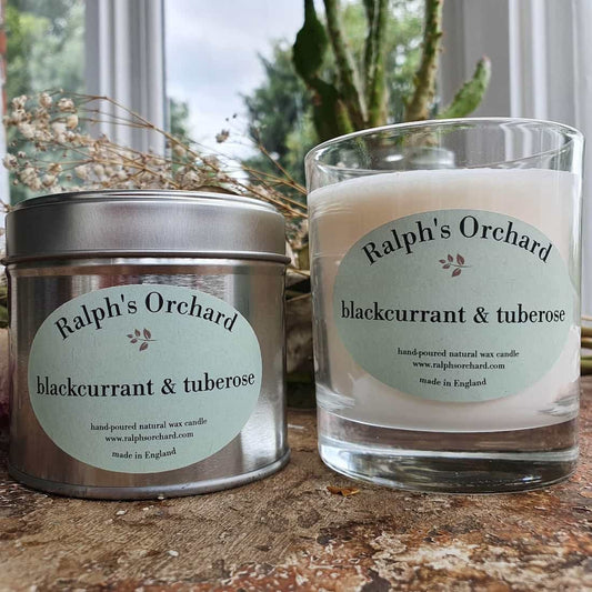Two candles labeled 'Ralph's Orchard' on a wooden surface with a blurred natural background.