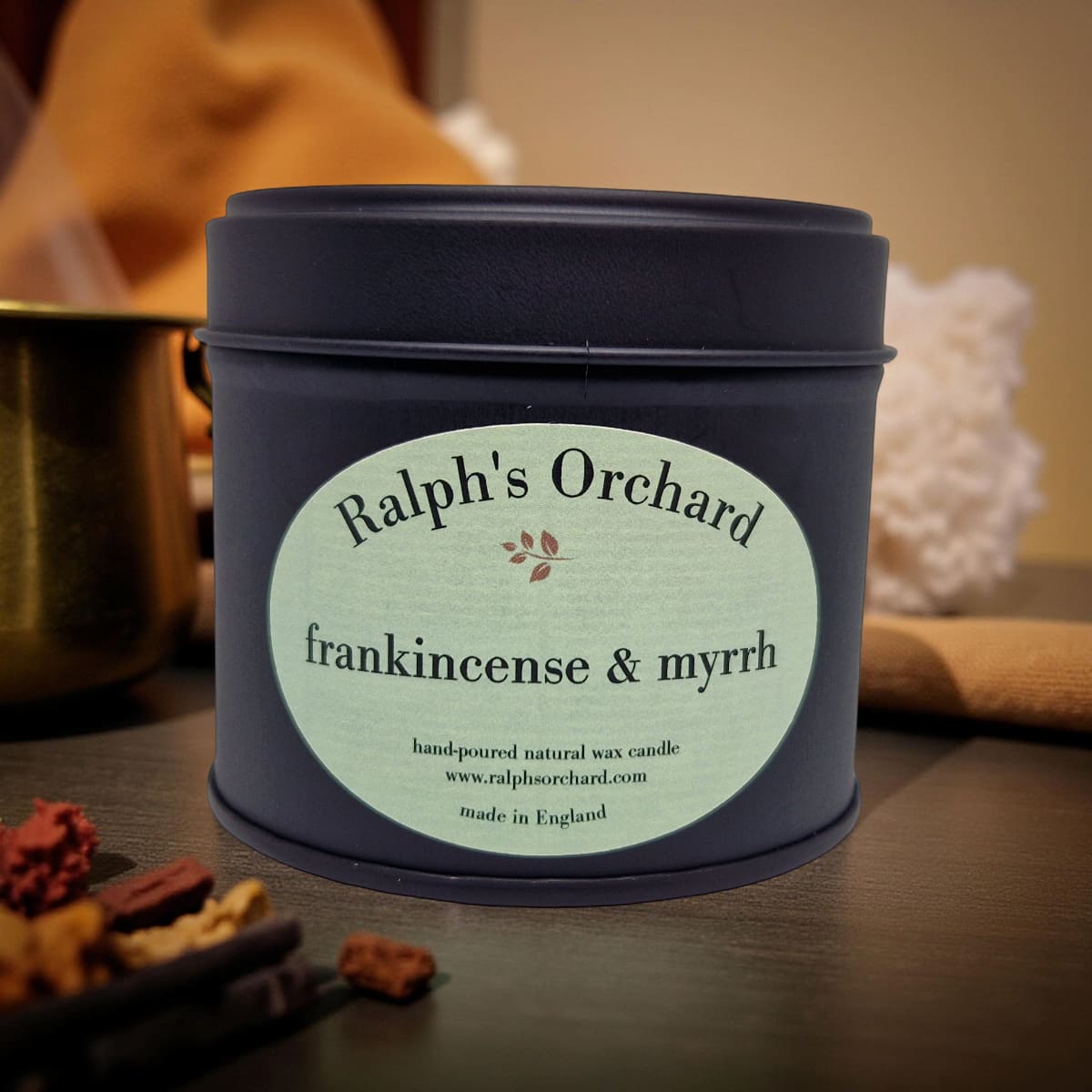 Candle tin labeled 'Ralph's Orchard frankincense & myrrh' on a wooden surface.