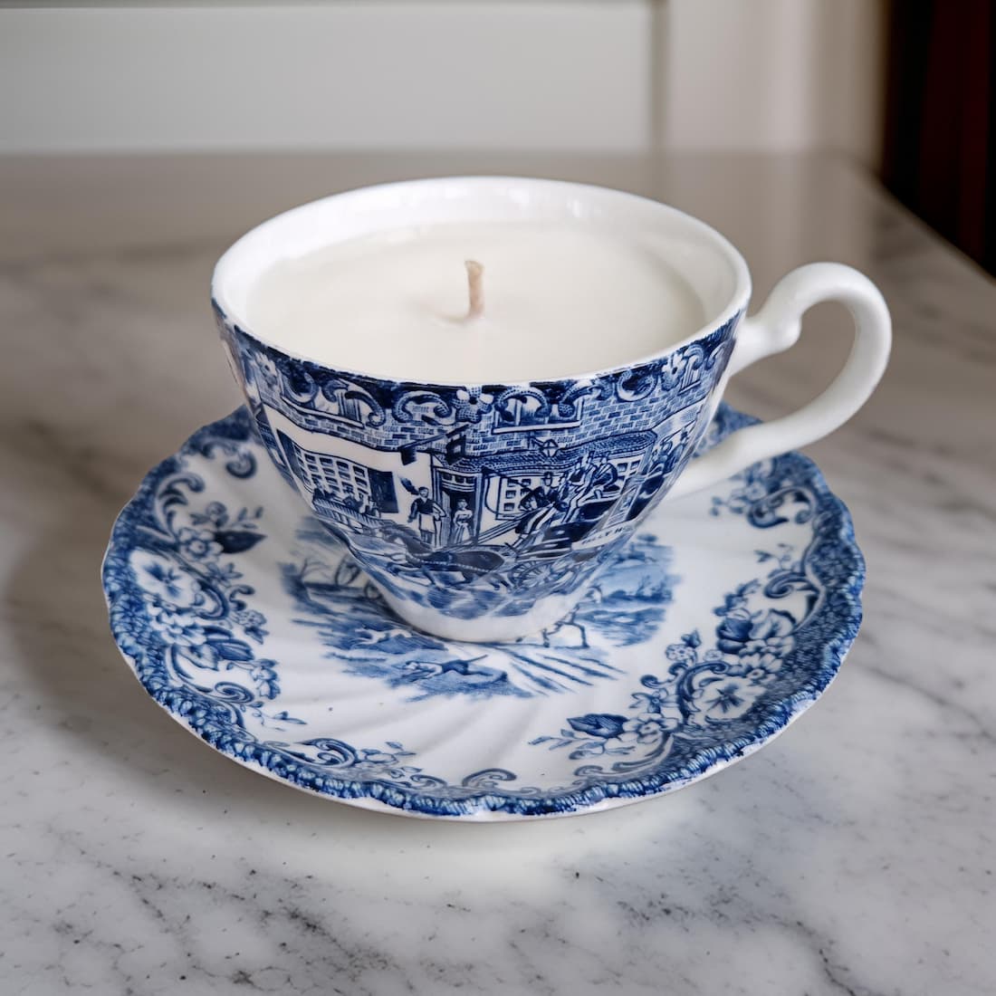 Blue and white teacup candle on a matching saucer on a marble surface