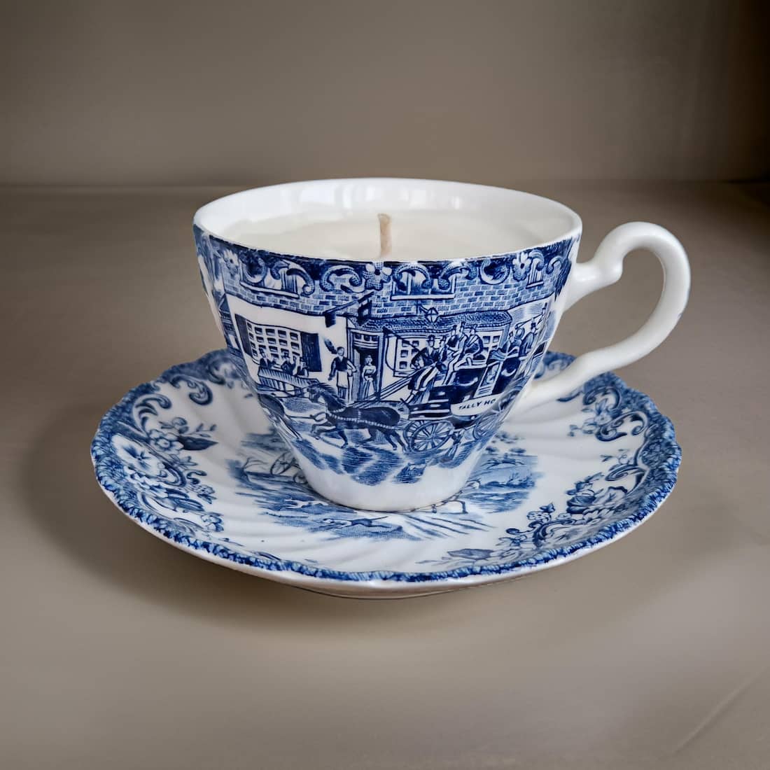 Blue and white teacup and saucer with a candle on a gray background
