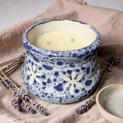 Ceramic candle holder with a candle inside, surrounded by lavender on a textured fabric background