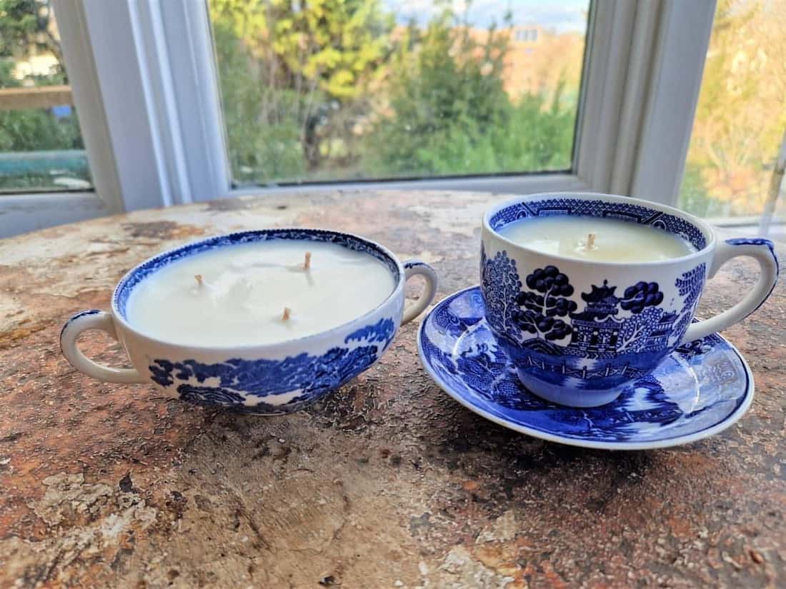 Two blue and white teacups with candles on a wooden surface, with a window view in the background.