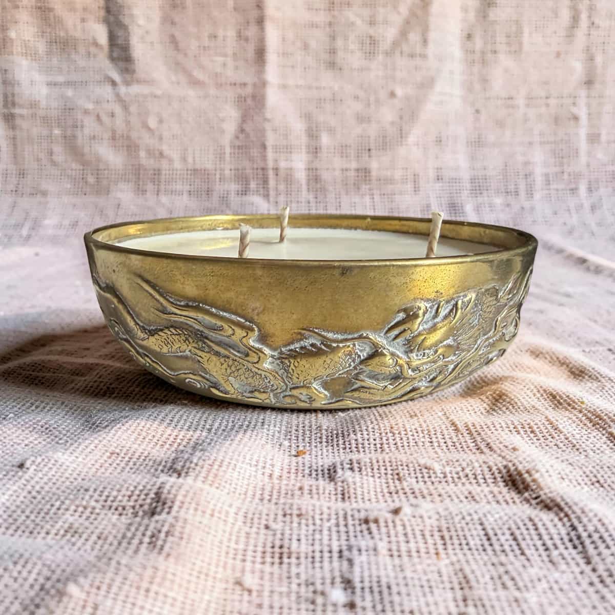 Decorative candle in a brass holder with embossed design on a textured fabric background