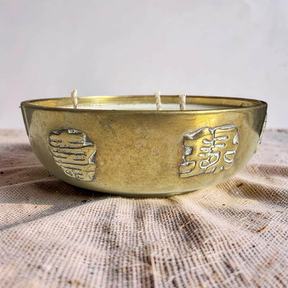 Brass bowl candle with embossed designs on a textured surface
