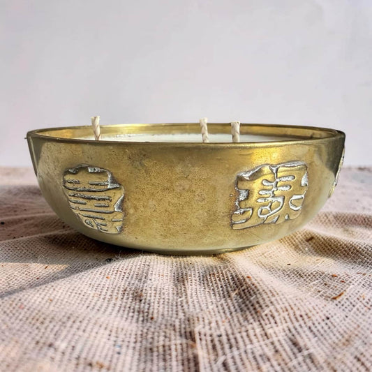 Brass bowl candle with embossed designs on a textured surface