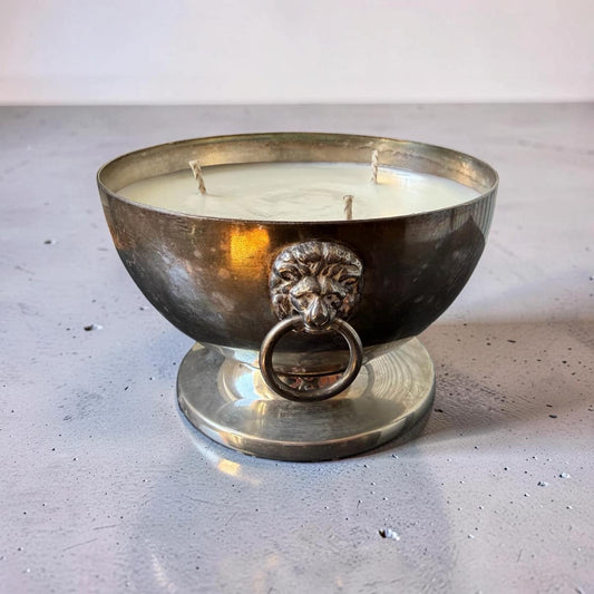 Decorative candle in a metallic holder with lion head design on a light background