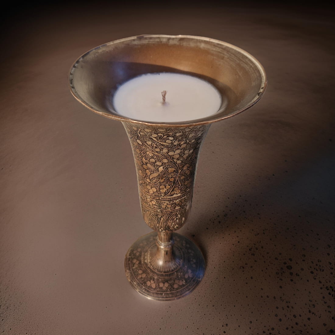 Decorative silver candle holder with a lit candle on a dark background