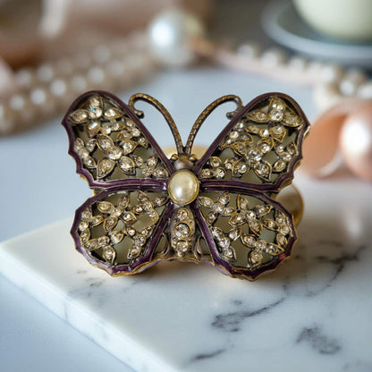 Butterfly-shaped jewelry box with rhinestones and a pearl on a marble surface.
