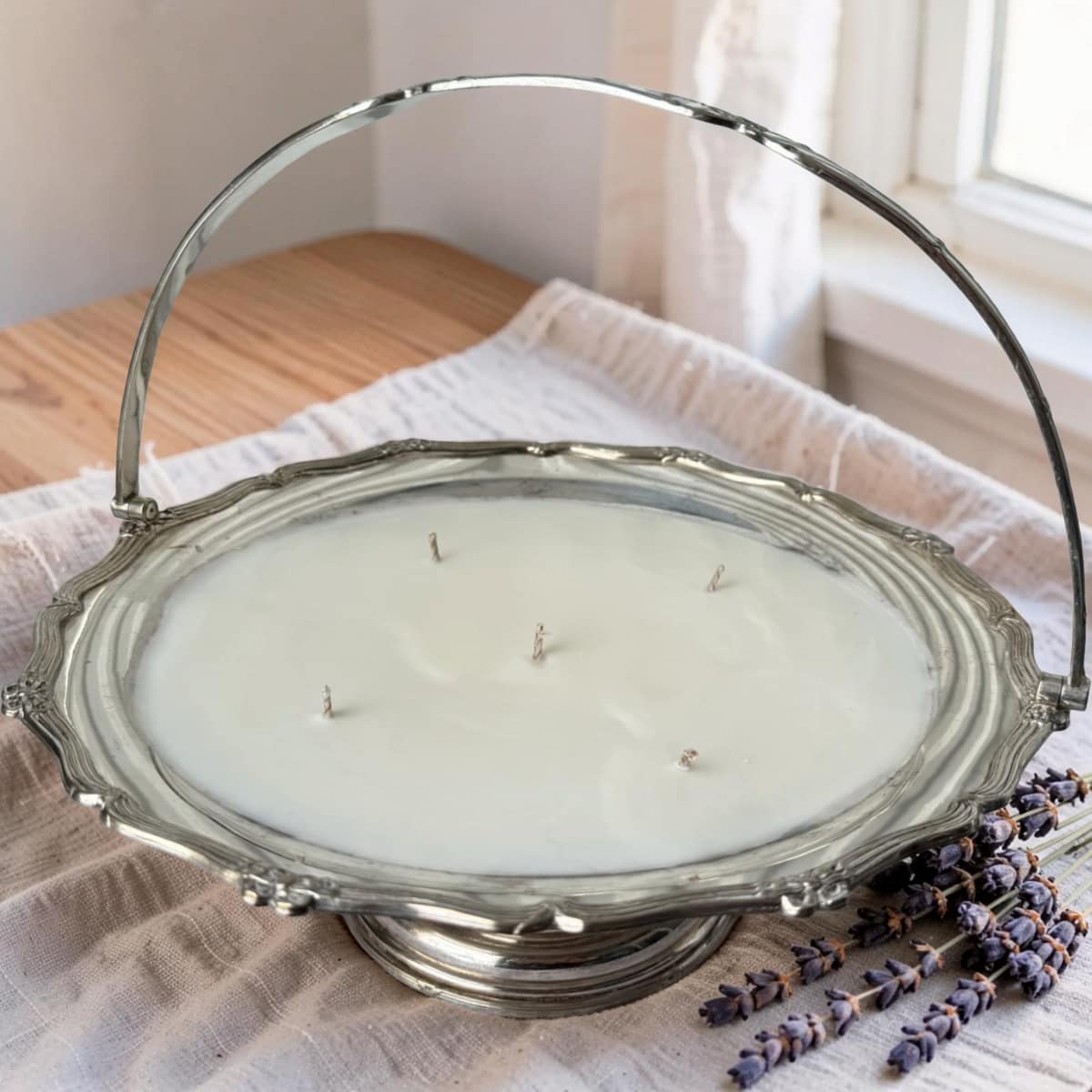 Decorative candle in a silver holder on a wooden surface with lavender flowers.