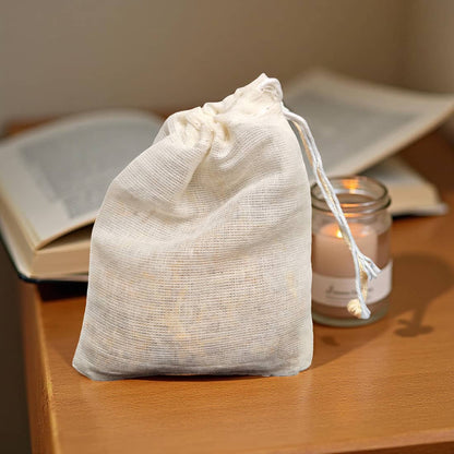 White drawstring bag on a wooden surface with books and a candle in the background