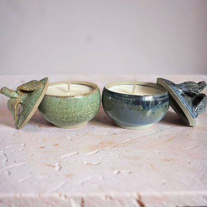 Two ceramic candle holders with lids on a textured surface