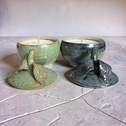 Two ceramic candle holders with candles inside on a textured surface.