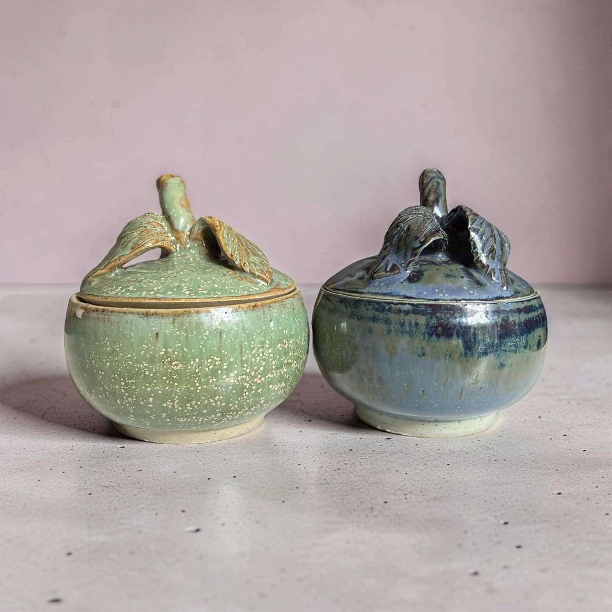 Two ceramic containers with lids on a light surface and pink background