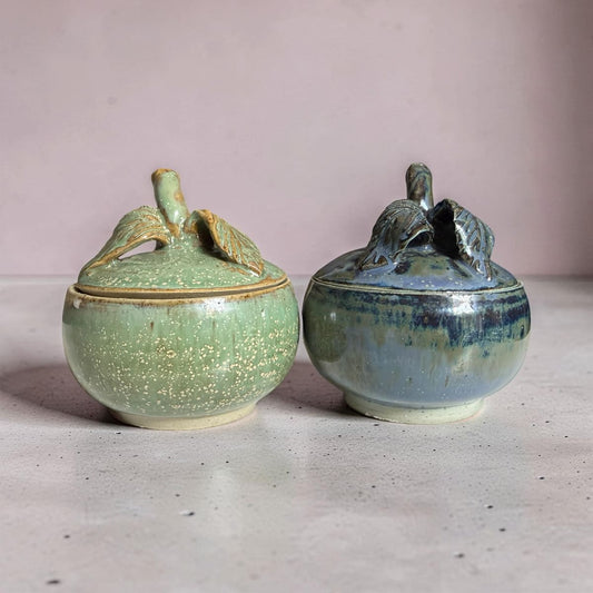 Two ceramic containers with lids on a light surface and pink background