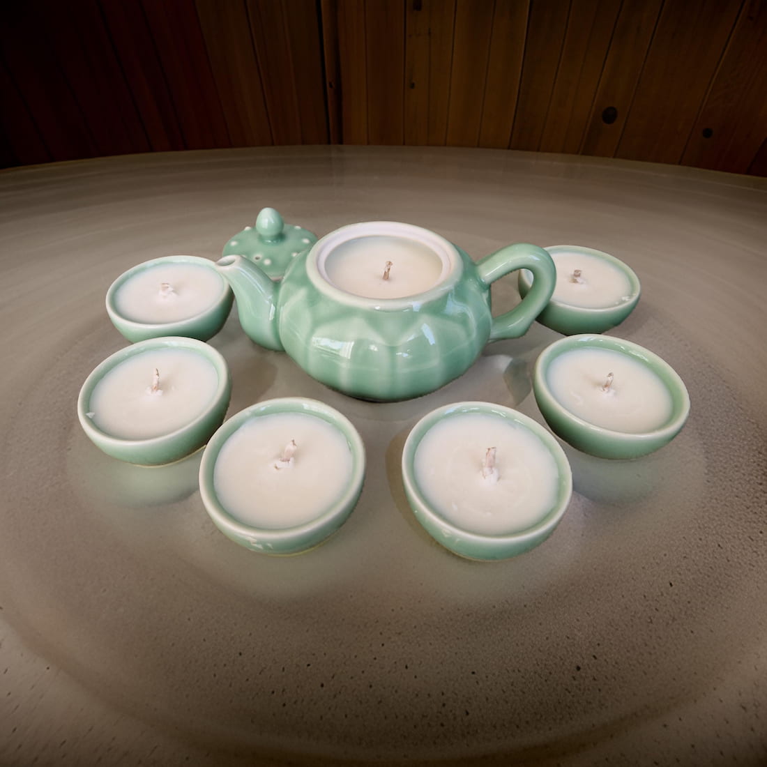 Green ceramic teapot with matching candles on a reflective surface