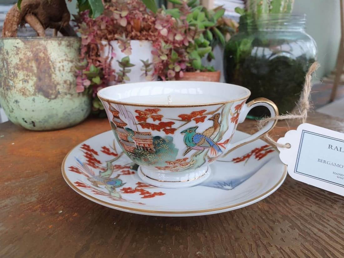 Teacup with decorative design on a saucer, placed on a wooden surface with plants in the background.