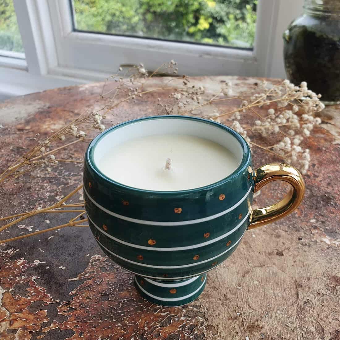 Green ceramic cup with a candle inside on a wooden surface with dried plants.